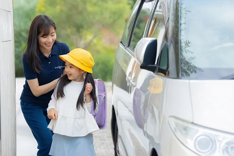 キュリオキッズの日本人講師が黄色い帽子の子どもと車に乗り込む