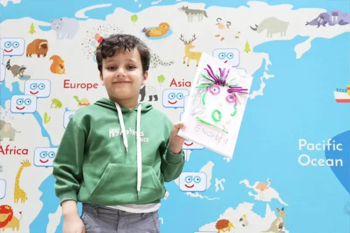 キュリオキッズの子供が世界地図の前で絵を持って立っている